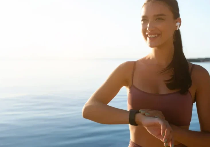 Woman smiling by the sea, wearing smartwatch.